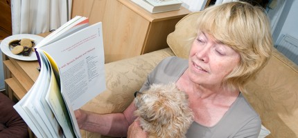 A lady reading a book with a fluffy dog on her lap.