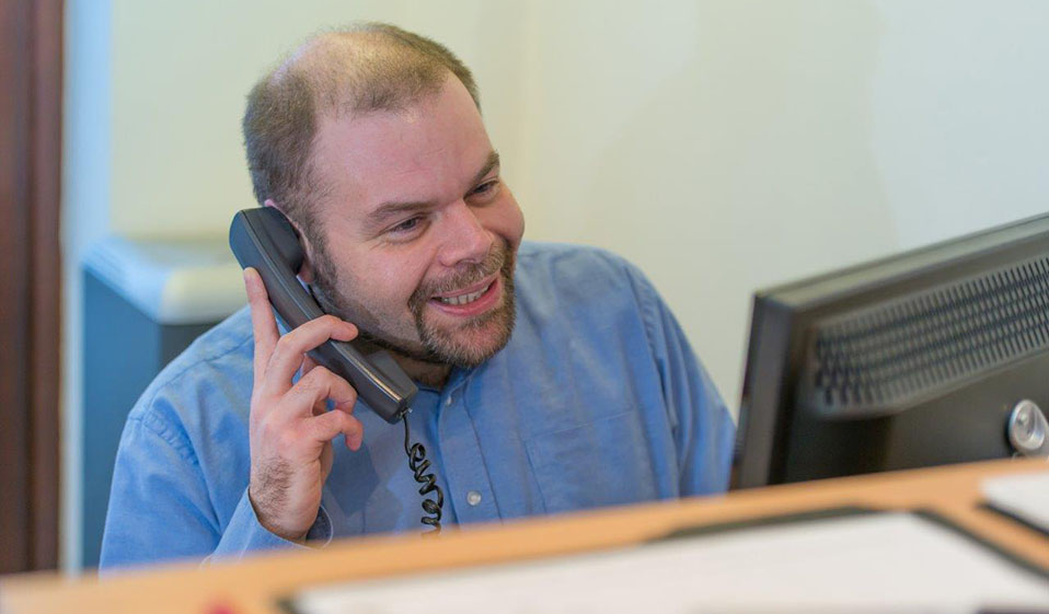 A man dressed in a blue shirt answering a telephone