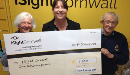 A couple presenting a cheque for £1000 to iShightCornwall's CEO, Terri Rosnau-Ward, wearing a black jacket.