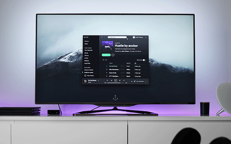 A flatscreen television displaying the Spotify music player interface. A mountain can be seen in the background.