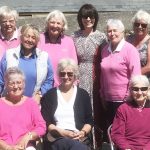 A group of women all smile at the camera. Some are wearing jackets with the Cape Cornwall Club logo on it. Another woman stands in the middle - this is Carole from iSightCornwall.