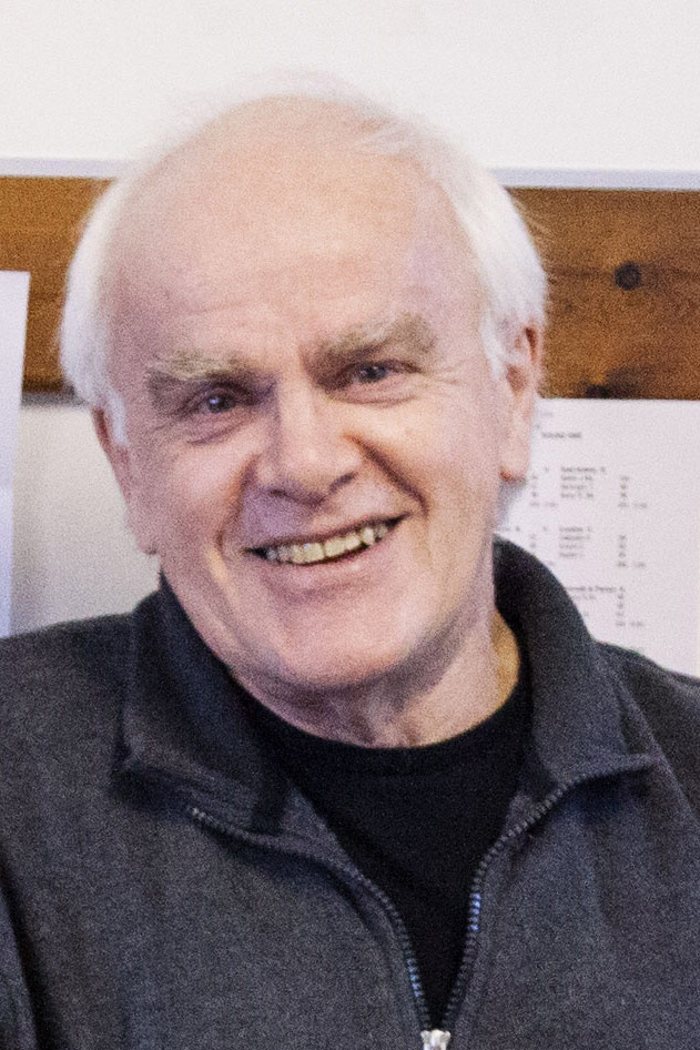 Close up of a man smiling wearing a grey zip up top and black tee shirt.
