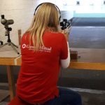 A female volunteer from Cornish Mutual aiming a rifle down a rifle range.