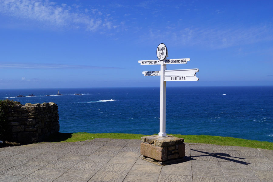 The Land's End sign in Cornwall. The ocean can be seen in the background and a clear blue sky.