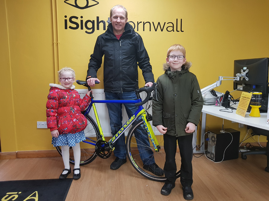 Craig Hancock and his two children stood in front of a bike inside the reception area of the Sight Centre. Craig is taking part in a charity cycle challenge from John O'Groats to Lands End.