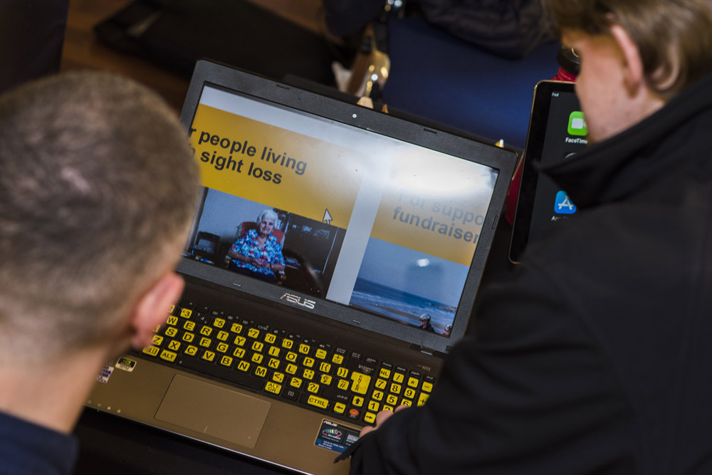 Two gentlemen looking at a laptop with yellow keyboard stickers and a zoomed in image of an iSightCornwall web page