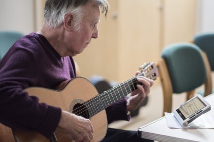 Michael, organiser of the Visually Impaired Guitar Club pictured playing a guitar with assistance from an electronic magnifier.