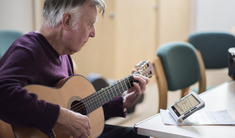 Michael, organiser of the Visually Impaired Guitar Club pictured playing a guitar with assistance from an electronic magnifier.