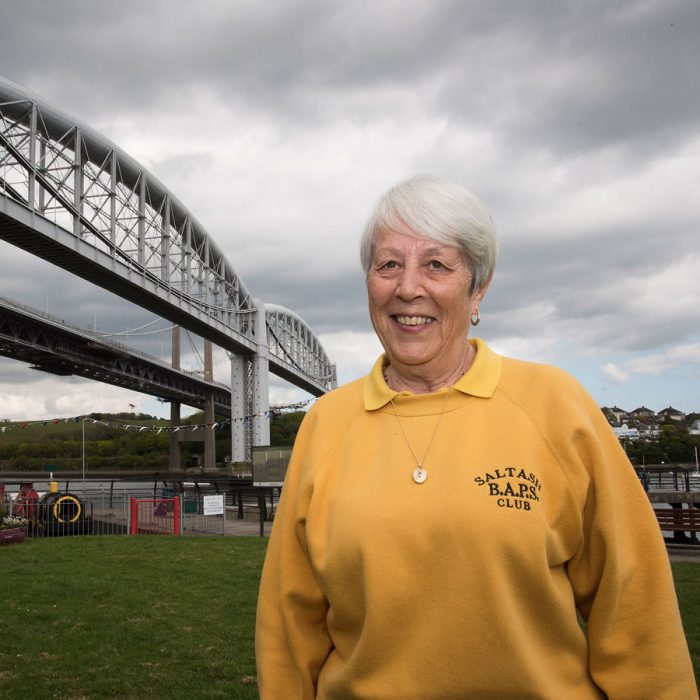 A lady in a yellow 'Saltash BAPS Club' branded jumper pictured underneath the Tamar Bridge connecting Cornwall to Devon.