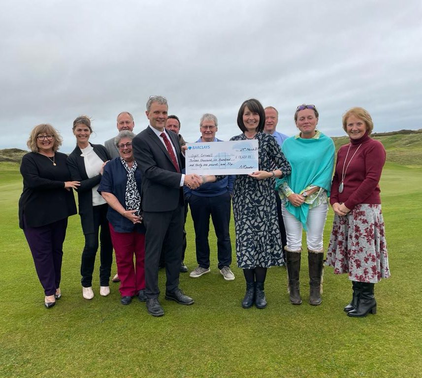 Members of the golf club stand on the green smiling for the camera. In front of them stands a man in a suit holding a cheque. On the other side is a smiling woman accepting the cheque.