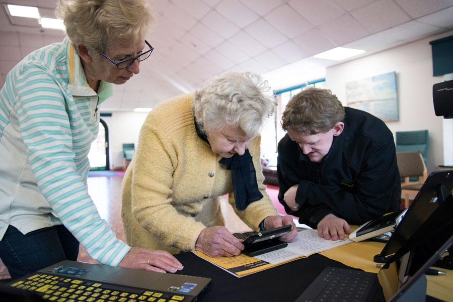 iSightCornwall Customer Services Advisor, Dominic Hall demonstrates an electronic magnifier to two ladies.