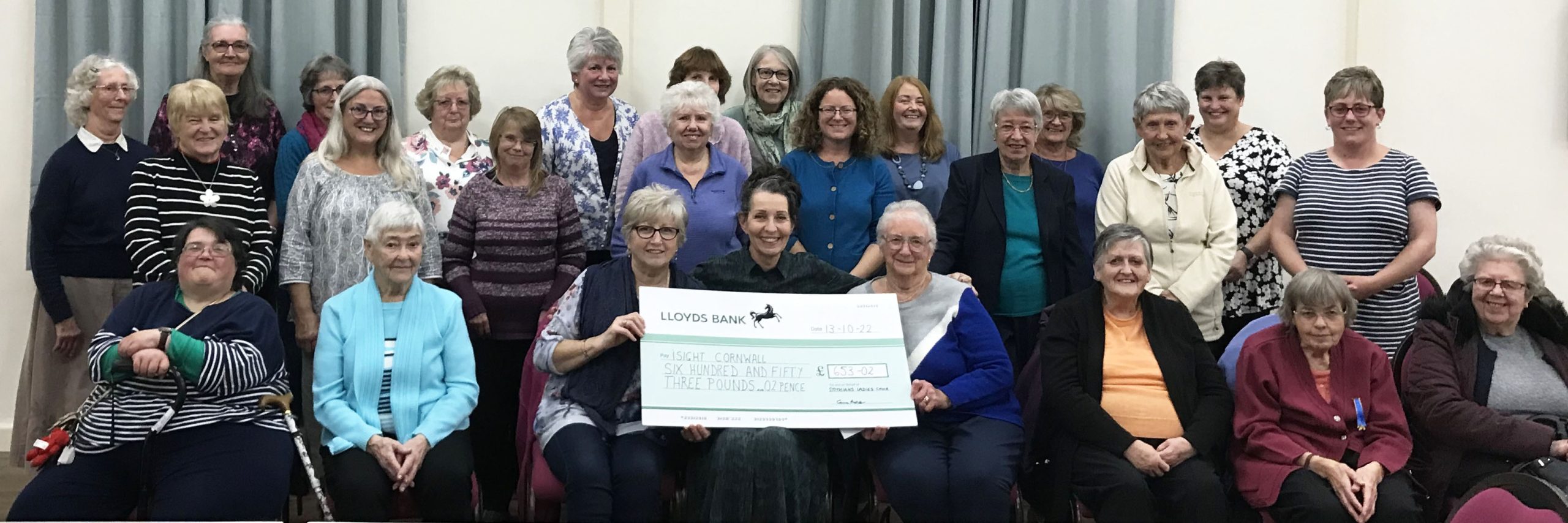 the members of the choir pose with a giant cheque and iSightCornwall's Carole Theobald