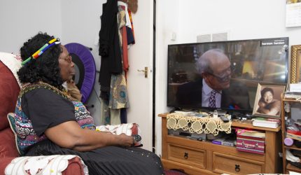 A woman sits close to the television, watching it intently