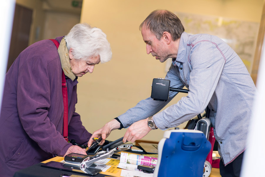 Rod from iSightCornwall demonstrates a handheld magnifier to a lady in a purple coat.