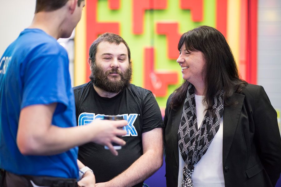 A man in a black tee shirt laughing with iSightCornwall's CEO, Terri Rosnau-Ward, wearing a black jacket whilst talking to a man in a blue tee shirt.
