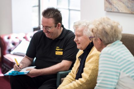 A man wearing an iSightCornwall branded polo shirt assists two clients in completing a questionnaire.